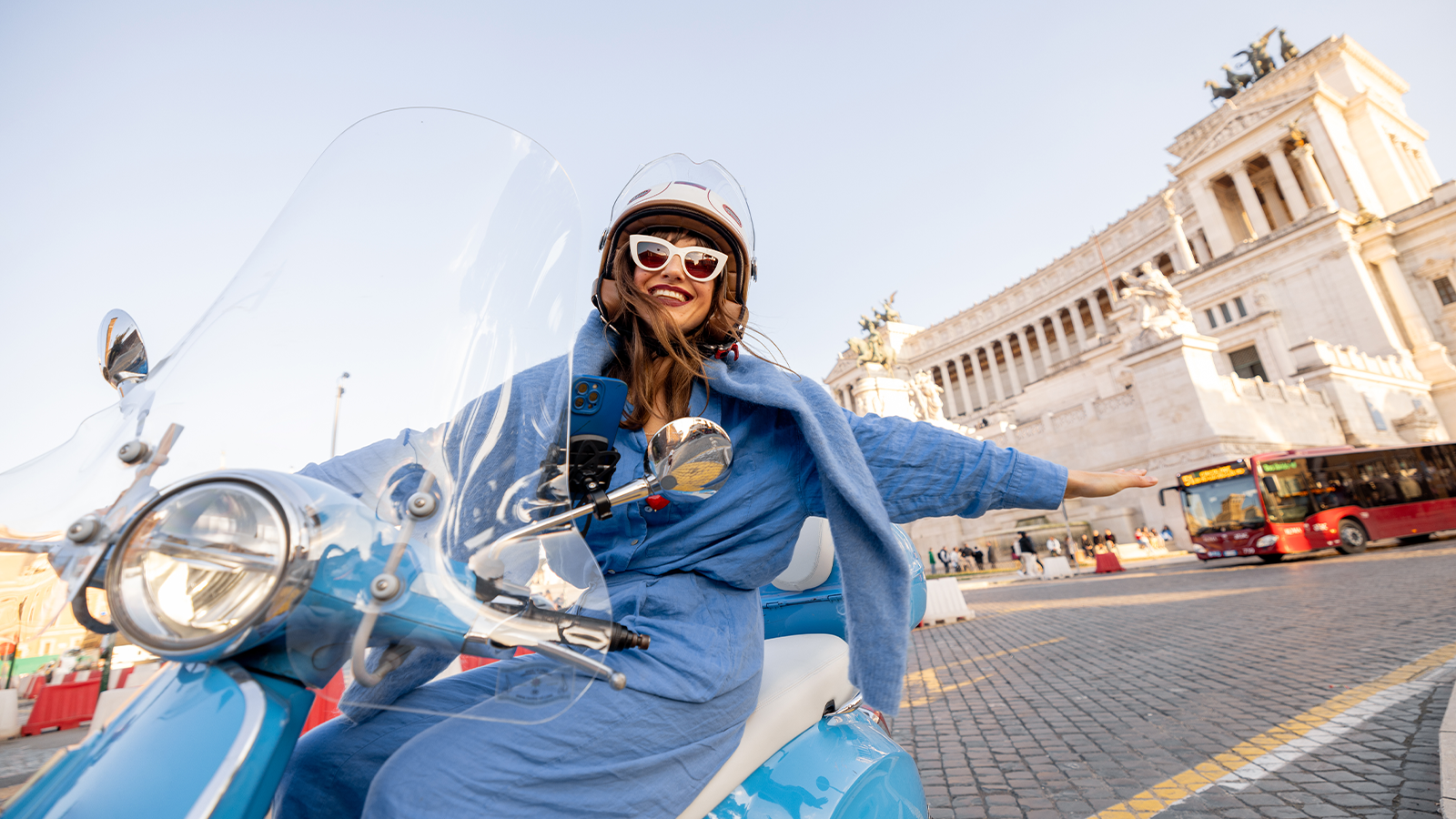 Vespa blu che attraversa una piazza monumentale di Roma